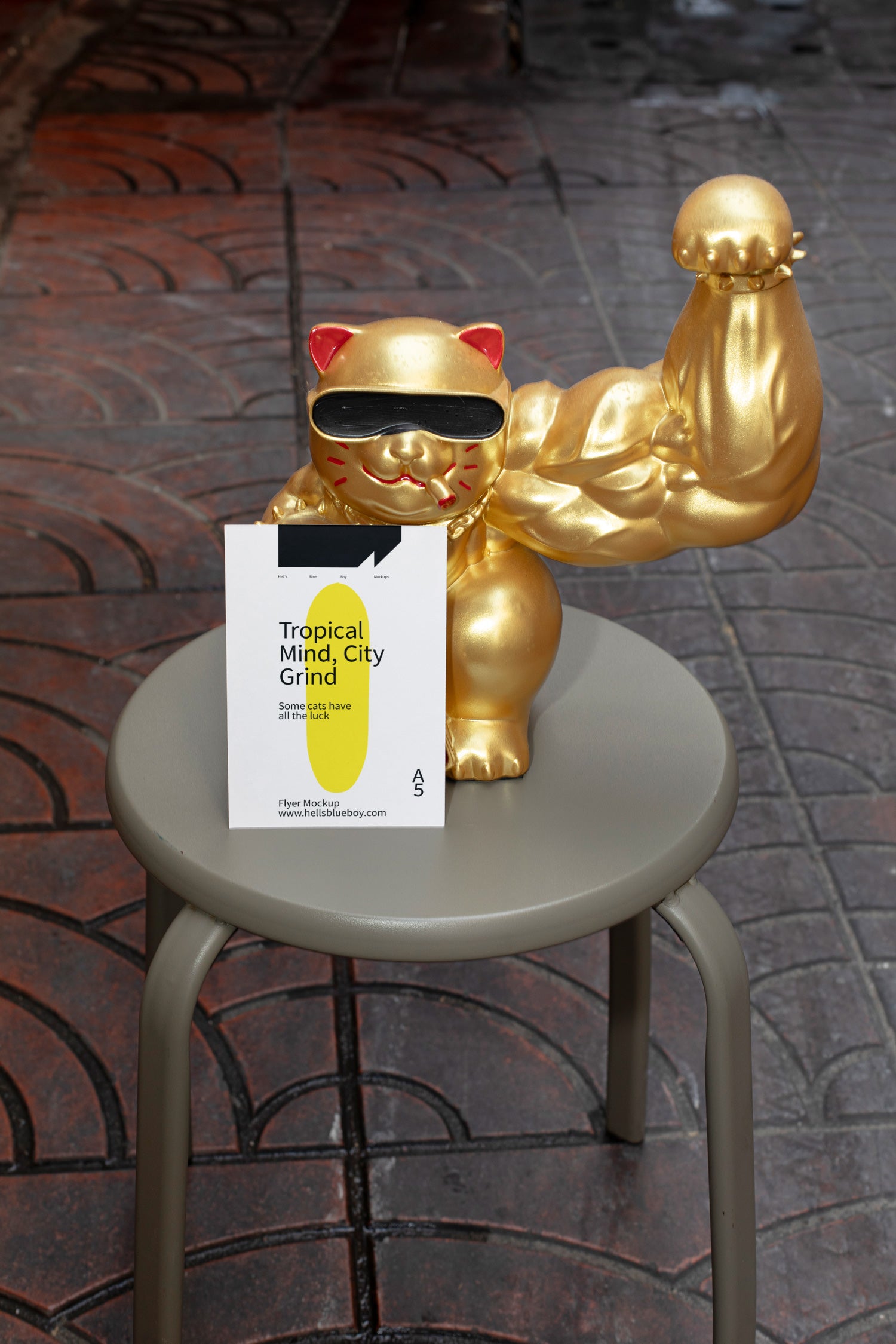 Street-style scene with a giant golden lucky cat sporting a muscular arm and holding a flyer, set on a chair against a tiled pavement background.